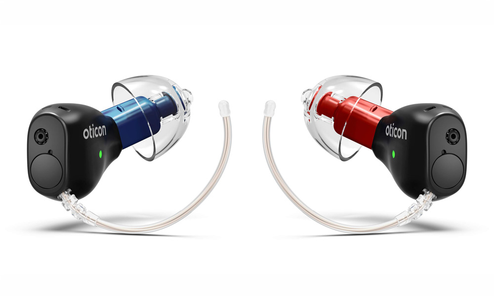Två svarta in-ear-hörapparater från Oticon med genomskinliga silikondomer. Den vänstra har en blå insida och den högra har en röd.