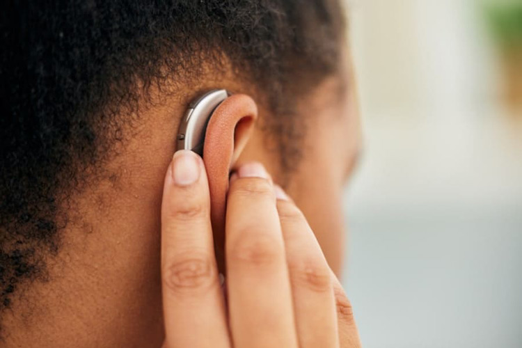 Närbild på en persons öra med en hörapparat placerad bakom örat. Personens hand rör vid eller justerar apparaten.