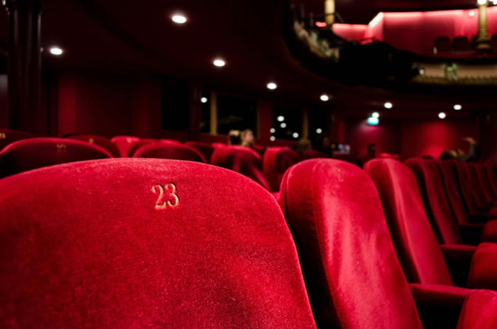 Röda sammetsstolar på rad i en teatersalong. På den närmsta stolen står siffran 23.