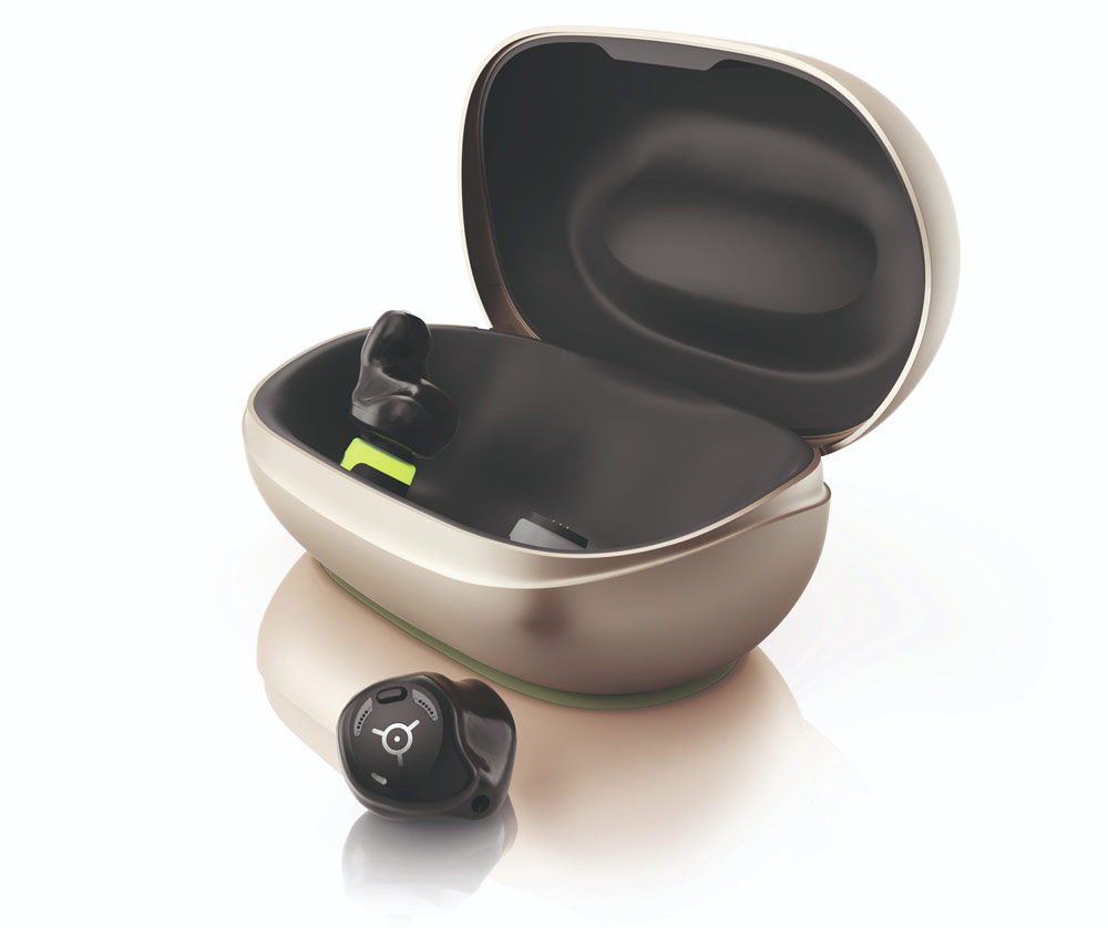Öppen laddningsetui i beige med svart insida för hörapparater; en svart hörapparat sitter i etuiet och en ligger framför på en ljus bakgrund.